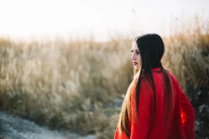 Side profile of a woman outdoors at golden hour, red jacket contrasting with tall dry grass.