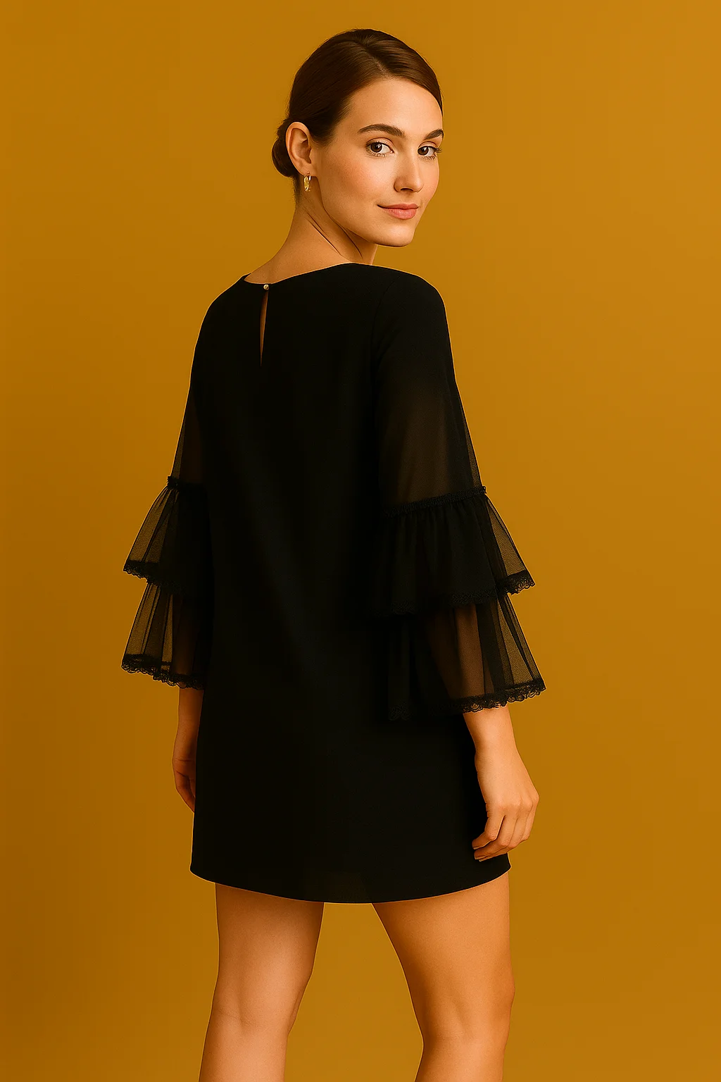 Back view of woman in a black mini dress with tiered sheer ruffle sleeves, standing against a warm mustard background.